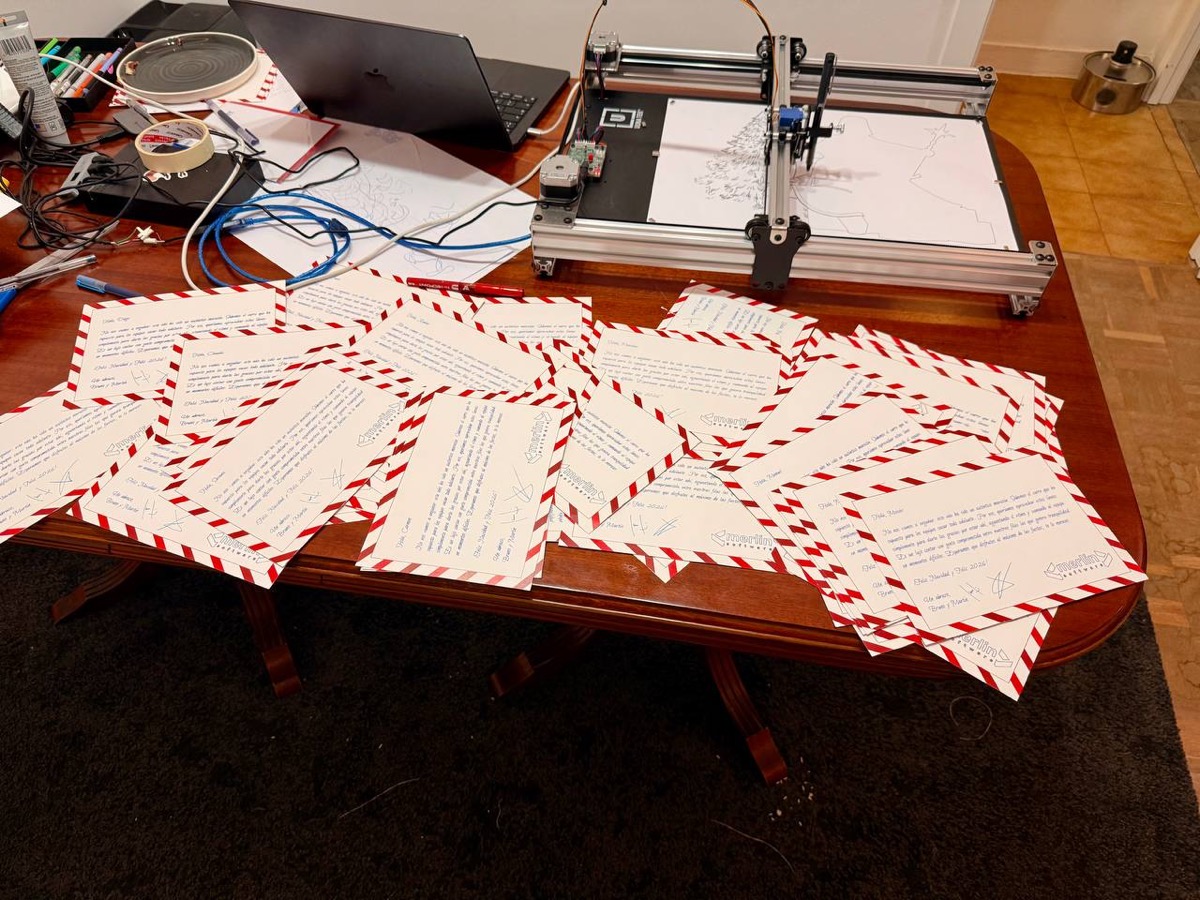 Dozens of personalized Christmas cards spread across a table, each with a red and white striped border, the plotter visible in the background.