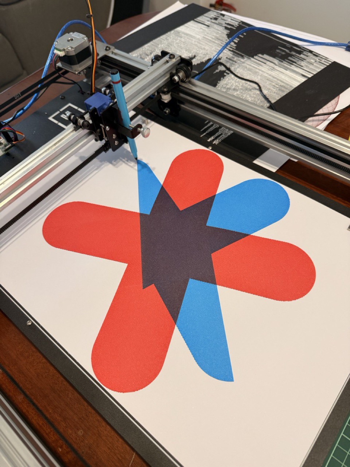 Logo filled with crosshatching in red and blue, plotted on the iDraw with a Joy Division print visible in the background.